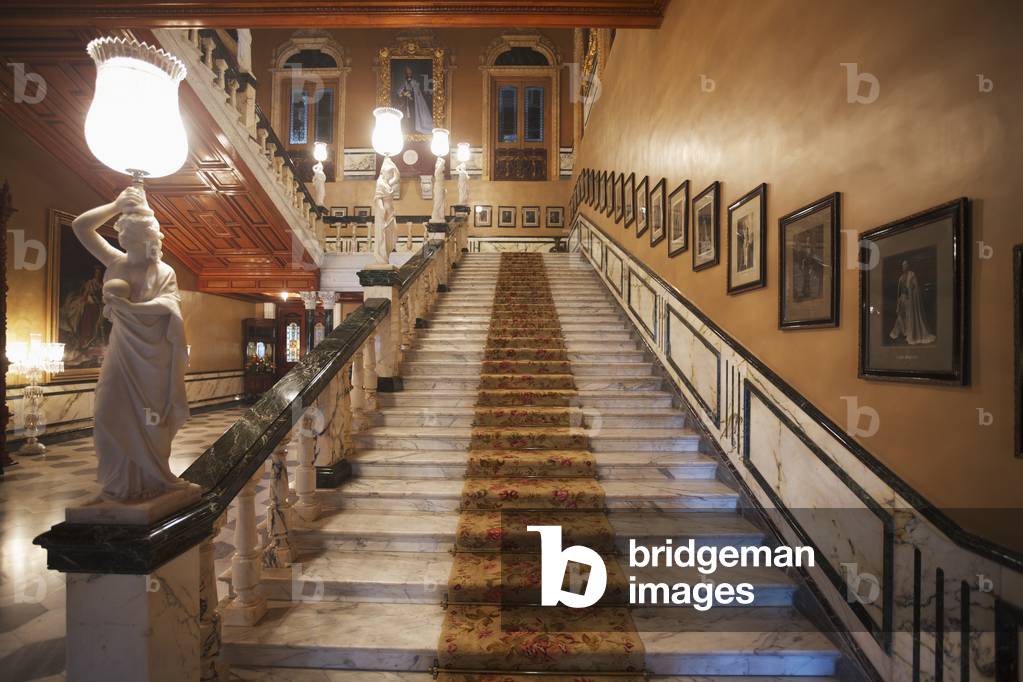 Staircase with photographs lining the wall and statues on the railing in Falaknuma Palace, Hyderabad, Andhra Pradesh, India (photo)