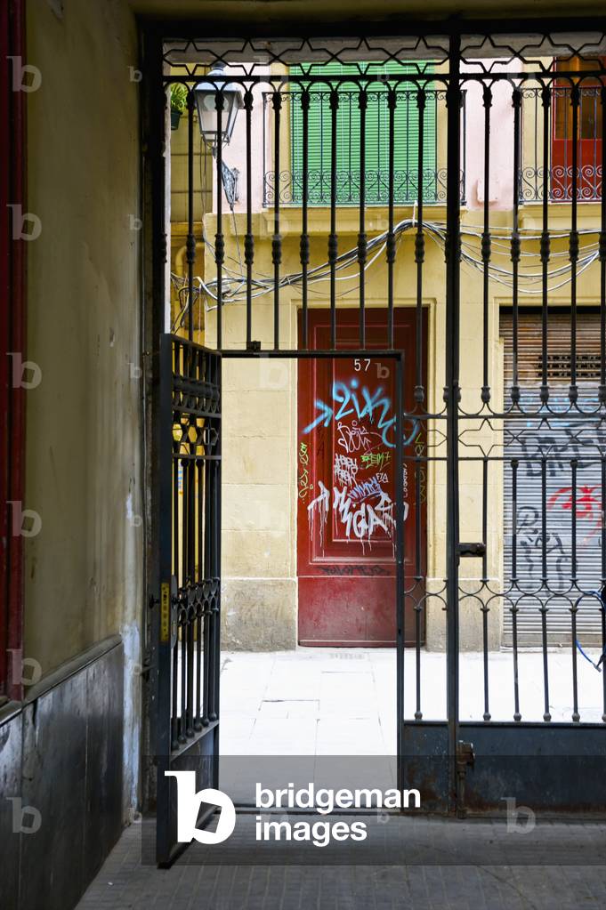 A metal gate open in the lower floor of a residential building with graffiti painted on the door across the street, Barcelona, Spain (photo)