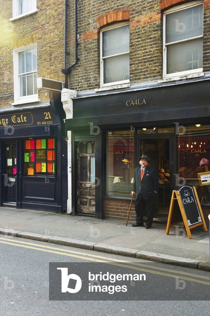 An elderly man with cane and top hat stands outside a restaurant, Shoreditch, London, England, UK  (photo)