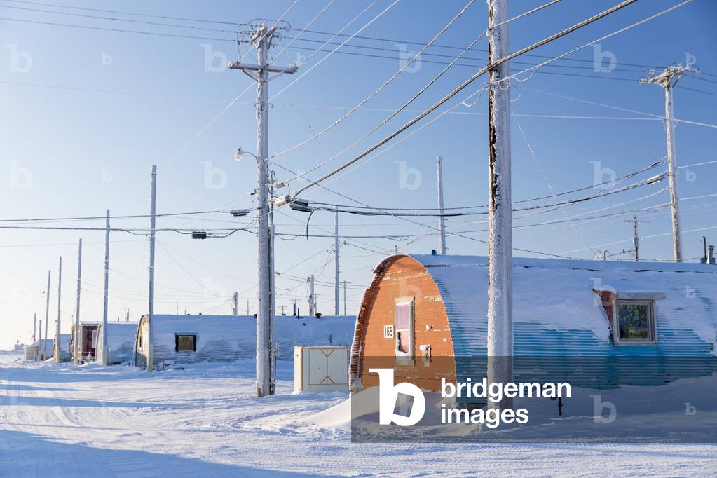 A row of powerlines stand beside Barrow Naval Base Quonset huts, Barrow, Arctic Alaska, Winter (photo)