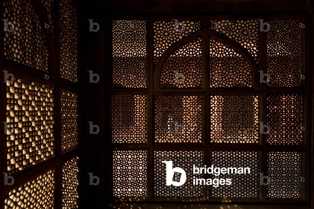Looking through stone lattice wall to man praying in the Jami Masjid, Fatehpur Sikri, Agra, India (photo)