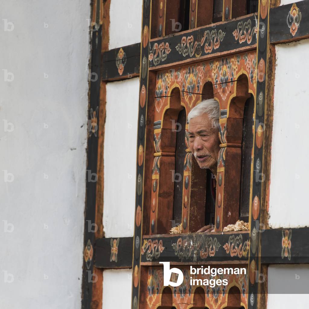 A man peers out a window from a wall with hand painted facade, Tachog Lhakhang Dzong, Paro, Bhutan (photo)