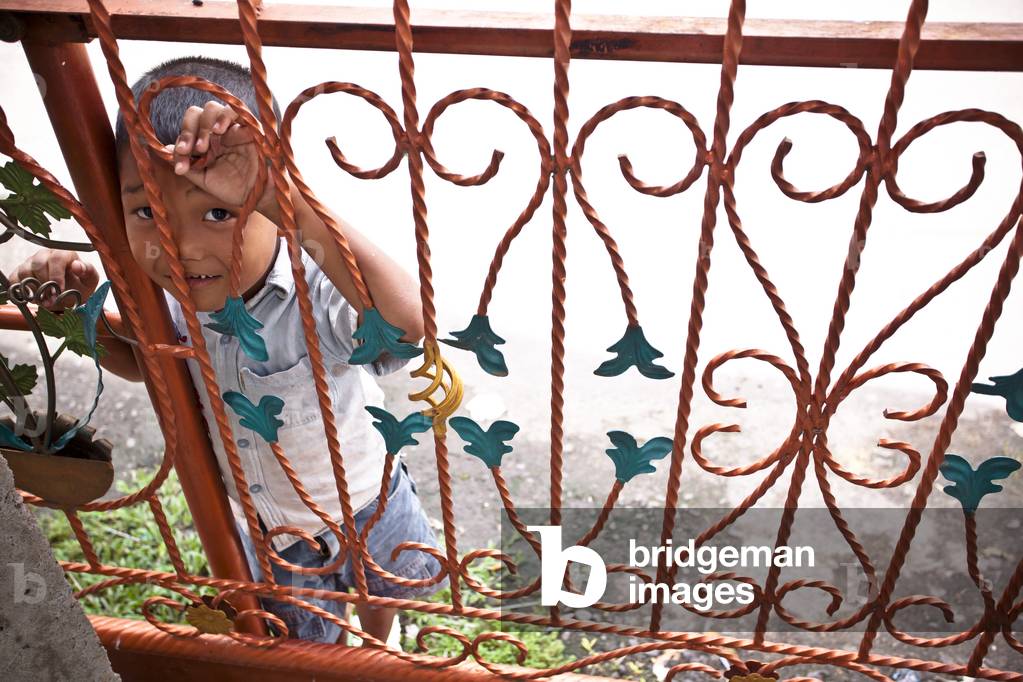 A Young Boy peeking through a Red Iron Railing, Sumatra Indonesia (photo)