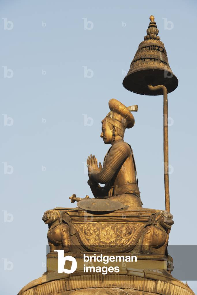 A gilded statue of King Bhupatindra Malla on a pillar with his hands folded in prayer posture, legs folded and a serpent supporting the capital, in front of the Golden Gate in Durbar Square, Bhaktapur, Nepal (photo)