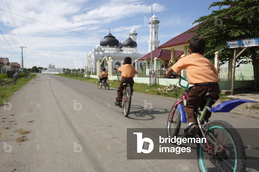 School children cycling along the road in front of a small mosque, near Banda Aceh, Aceh Province, Sumatra, Indonesia (photo)