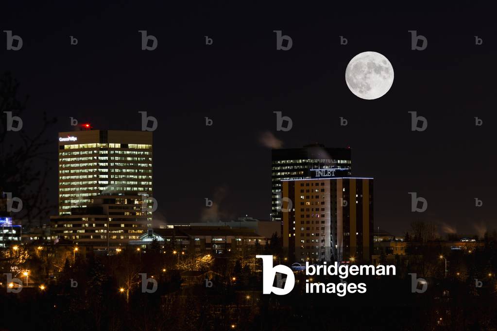COMPOSITE: A full moon hovers over the skyline of downtown Anchorage, Southcentral Alaska, Winter (photo)