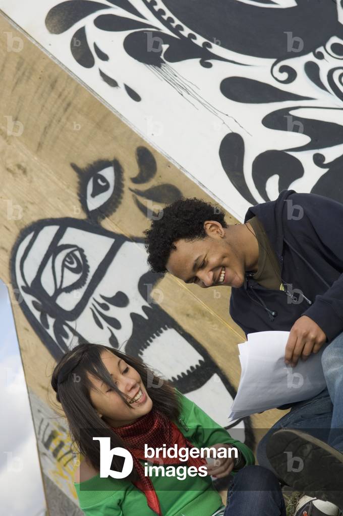 UK, Teenage girl and boy studying in front of graffiti wall, Hastings (photo)