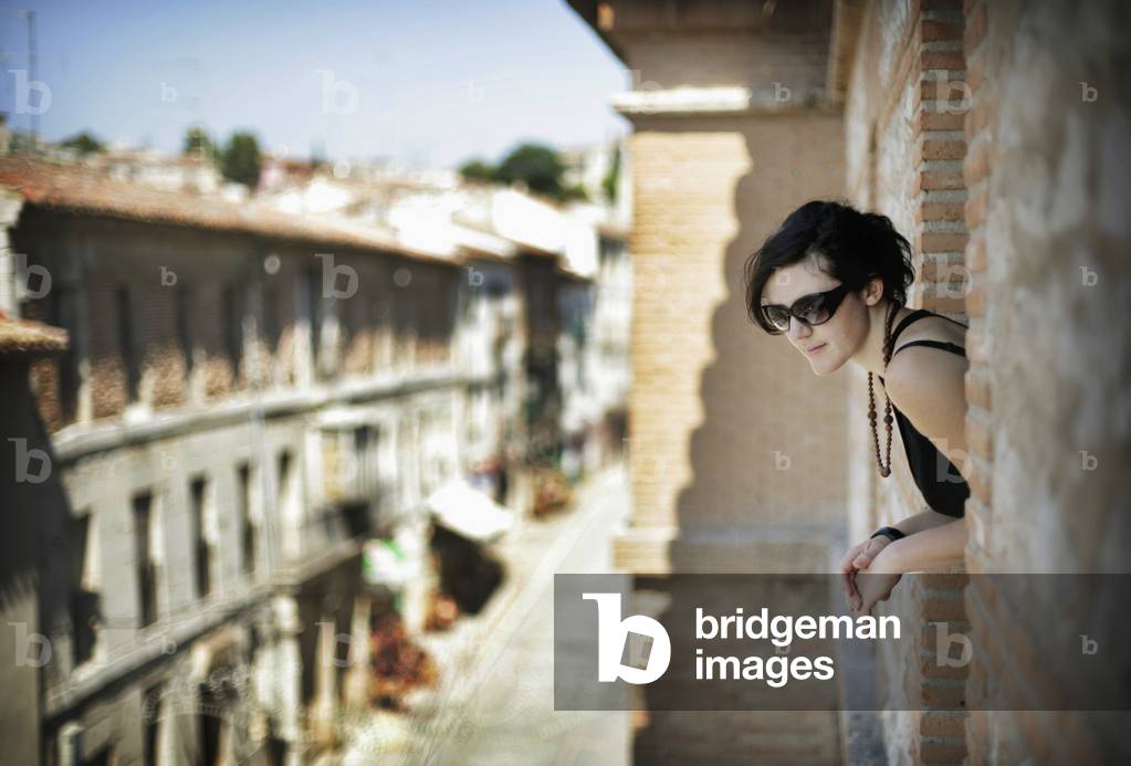 Young Woman Looking Out of Balcony Window in Parador Hotel, Chinchon, Spain (photo)
