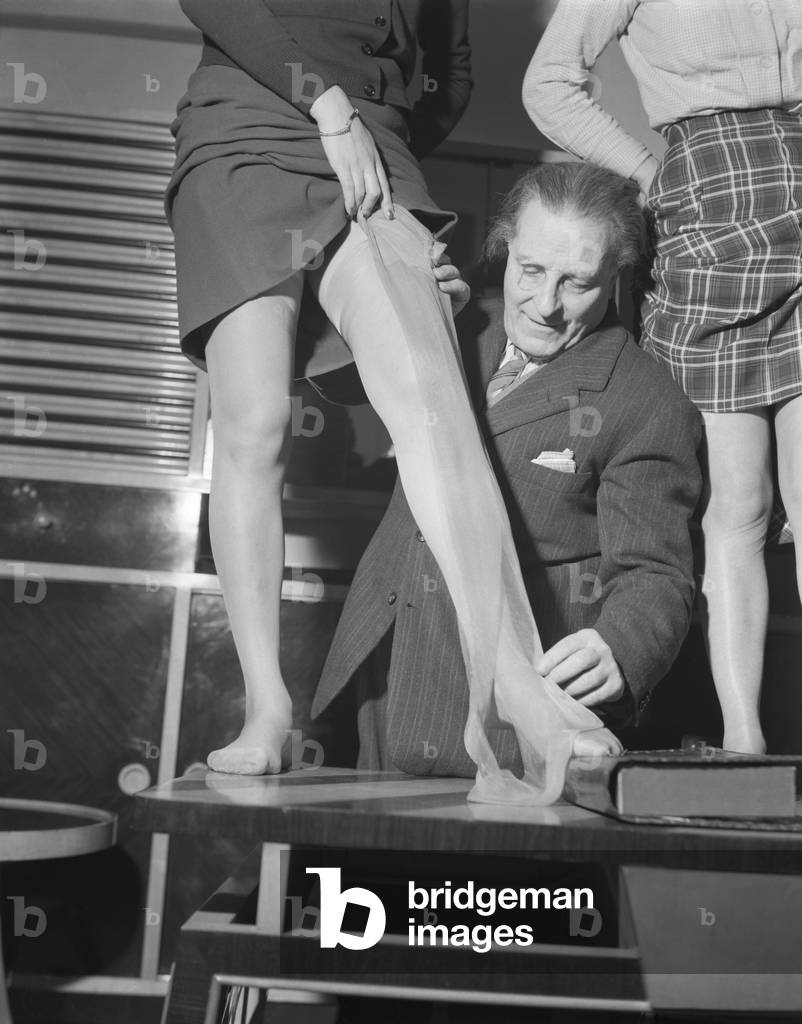A man displaying tights on a model standing on a table, Museum of Famous Tights, Milan, 1950 : Measuring Tights