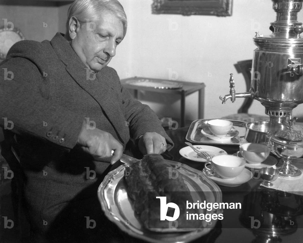 Italian painter Giorgio De Chirico, sitting at a table, wearing a blazer, cutting a strudel cake, on the table