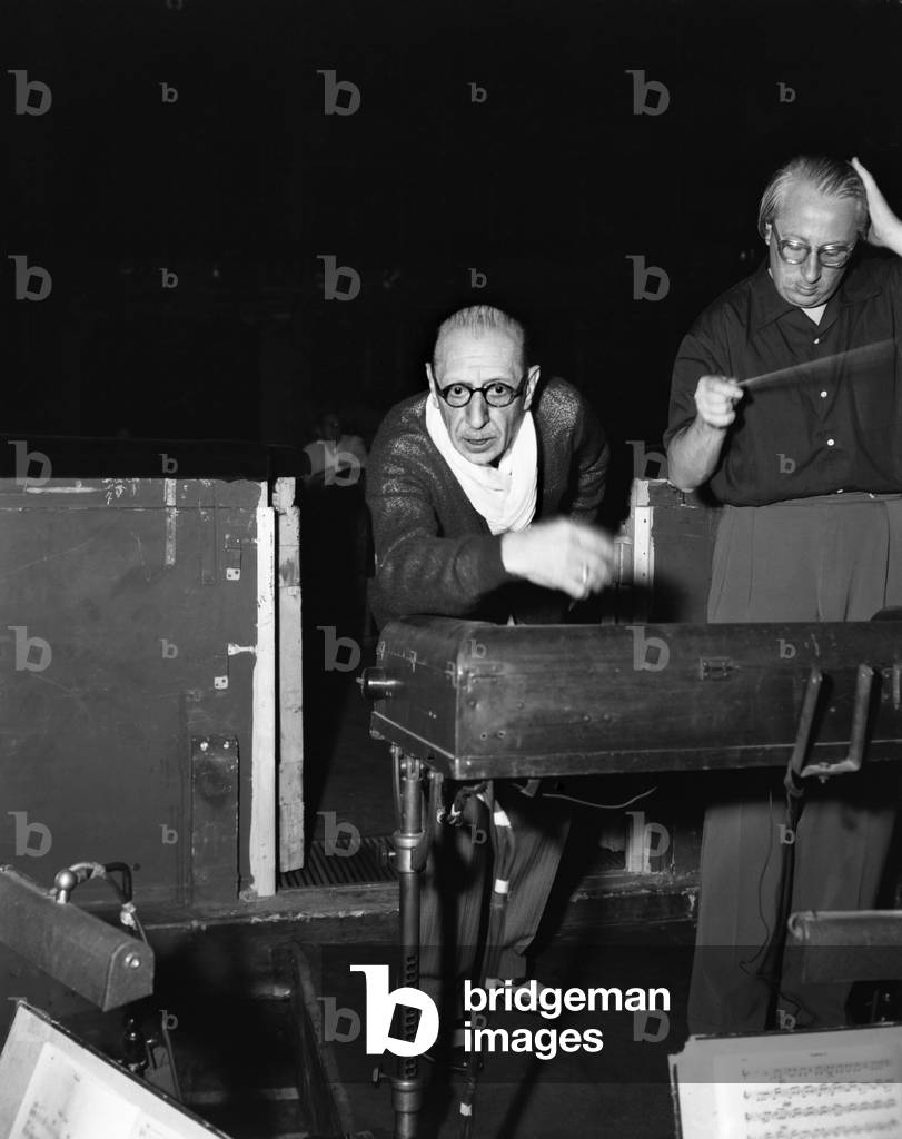 Russian composer Igor Fedorovich Stravinsky (Stravinski) conducting an orchestra at Fenice theater, wearing a woolen jumper, pinstriped trousers and two-tone shoes, a baffled man besides him, Venice, 1951