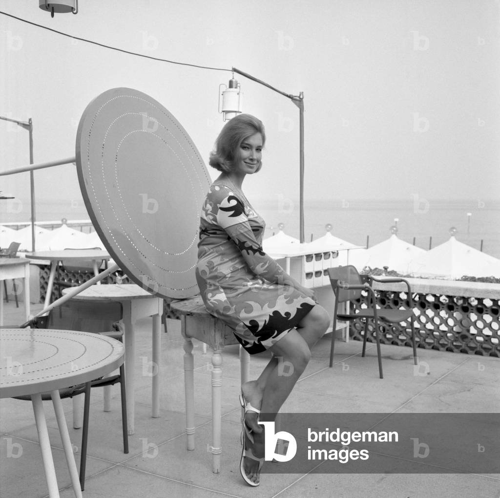 Italian actress Annabella Incontrera posing for the photographer while sitting on a table, the Lido beach in the background, Venice, 1967 : At Lido