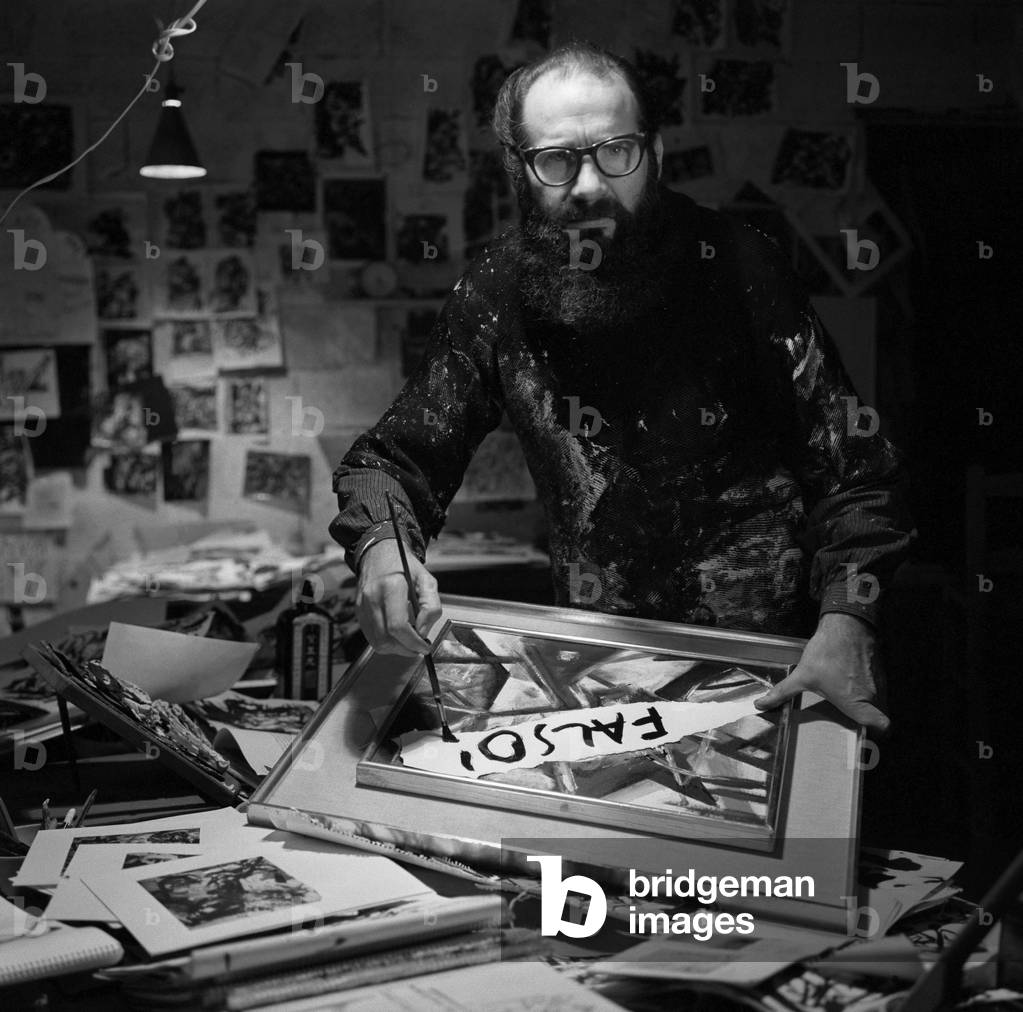 Italian painter Emilio Vedova, with his painting in his studio, wearing a paintstained shirt and glasses, holding a paintbrush, surrounded by drawings and sketches, Venice 1960s