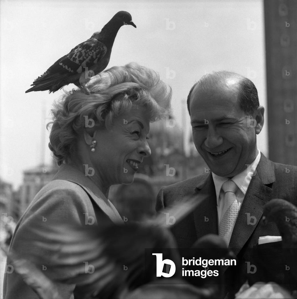 American art promoter David E. Bright and wife, a pigeon standing on her head, in St. Mark Square, in Venice for the Art Biennale 1958