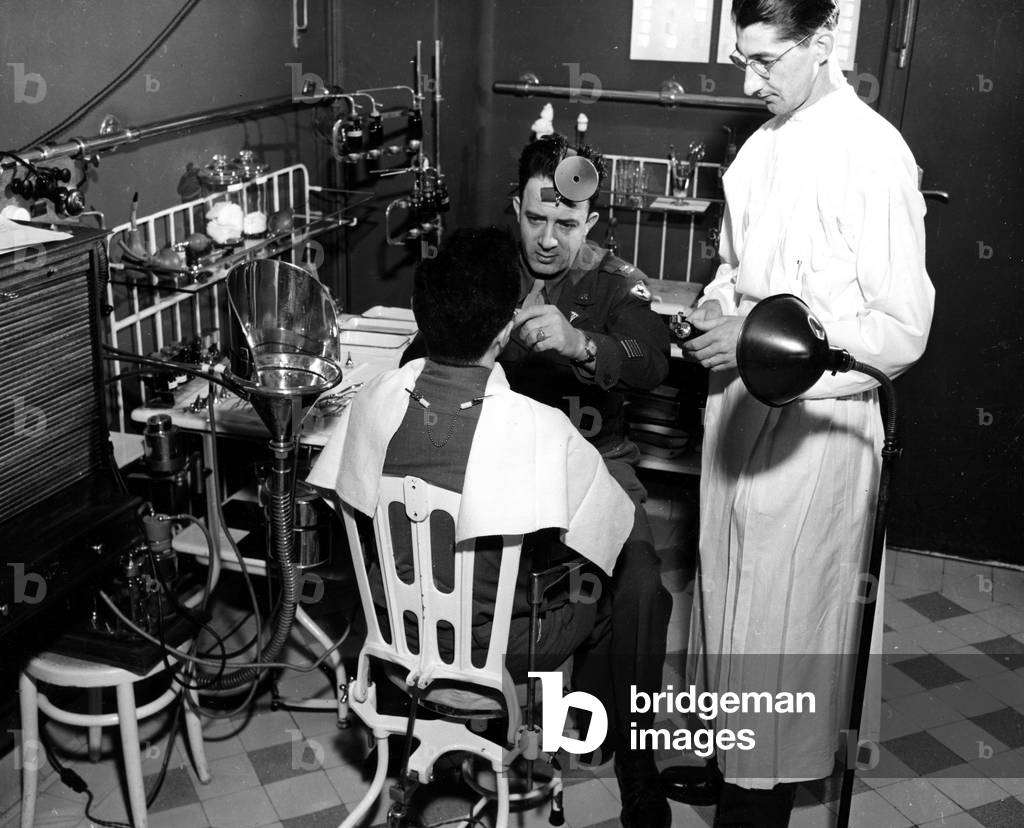 WWII:Neuilly sur Seine (France) March 1945: At the American Hospital which became the 365th Station Hospital of the American Armee, assisted by a nurse sergeant, a captain of the Service de Sante apprets to operate vegetations and tonsils an American soldier.