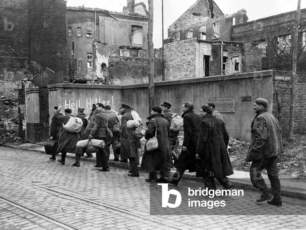 Second World War (1939-1945): French soldiers and workers required after the liberation of the city of Munchen-Gladbach (Munchen Gladbach) (present-day Monchengladbach (Germany) by elements of the 9th US Army - They pass before a wall inscribed “Heil Hitler!” Photography beginning March 1945