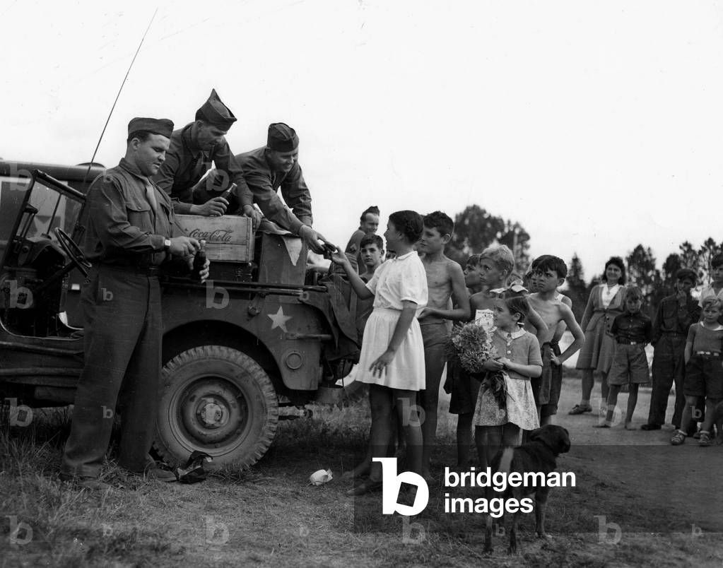WWII:Near Reims (Marne) France 7 August 1945: a “regate” of auxiliary reservoirs, American soldiers distribute donuts and Coca-Cola to young French