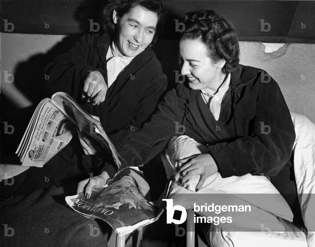 WWII:Barneville (Normandy) France March 10, 1945: At the 174th General Hospital, a nurse from the US Army (right) and a young French employee recovering for exhaustion compare their magazines