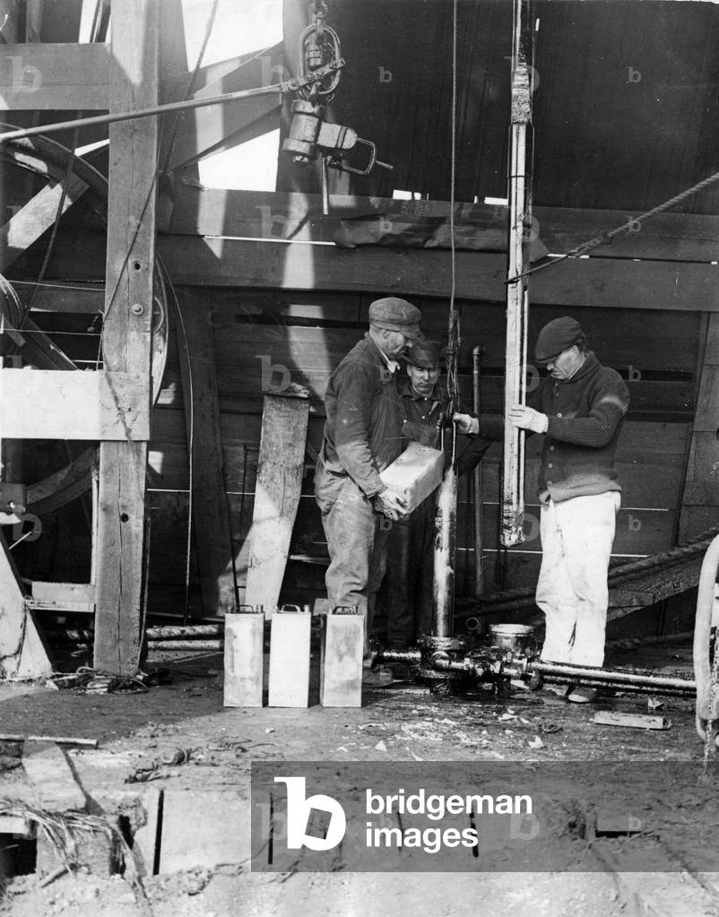 USA around 1925: Workers pour nitroglycerine into a “shell” that will burst into the sand at the bottom of a well to stimulate the flow of the oil.