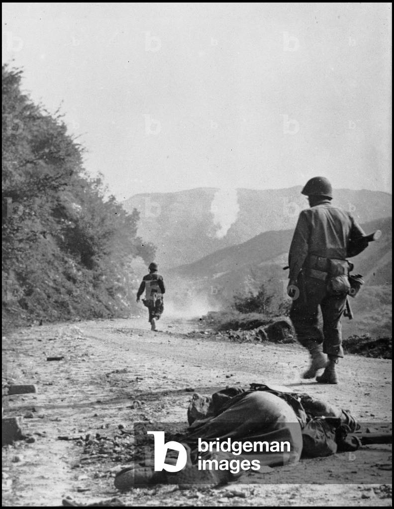 Second World War (1939-1945): North of Ponzalla (Northern Italy) October 1944. American soldiers from the Fifth Armee advance towards the Gothic Line. In the foreground, a dead German soldier and in the background, the smoke of a phosphorus shell indicates the battle line. Photography