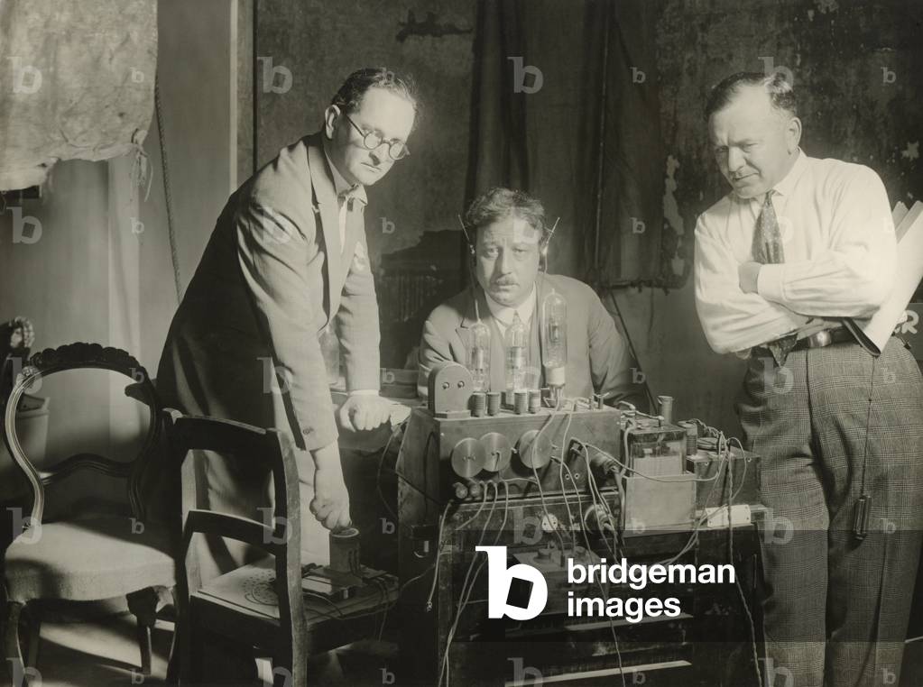 Inventor, Joseph Massolle (center), listening to the first screening of German Movietone News. He is using a machine called a Trigeron (Work of Three), invented in 1919 by himself and Josef Engl (left) and Hans Vogt (right). Their technology for a sound track on movie film became the industry standard in the 1920s.