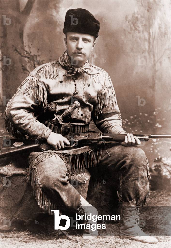 Young Theodore Roosevelt dressed in deer skins, posing with a rifle in an 1885 studio portrait