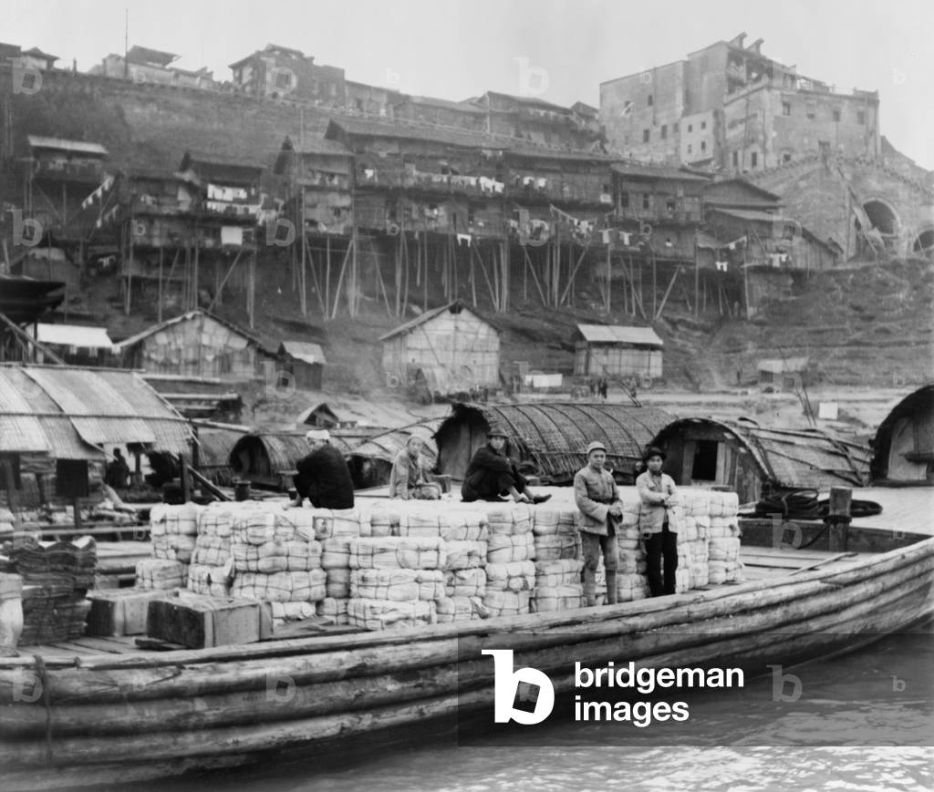 The riverfront of Chungking, China in Jan. 1944. As the inland wartime capital of China, it absorbed over a million refugees. Wooden barge is at dock with cotton bales. In the background are dwellings on the river bank. Second Sino-Japanese War/ World War 2