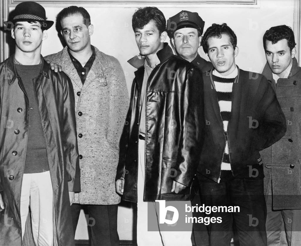 Teenage members of the Brooklyn Puerto Rican gang the Mau Maus, arrested in the fatal shootingof a rival gang member, Anthony Labanchino. Left to right, Carl Cintron, Patrolman Ernest Fatoruso, Carlos Reyes, Patrolman Frank Collins, Melvin Torres and Israel Narvaes (gang leader), at the Poplar St. police station, New York City. February 1959