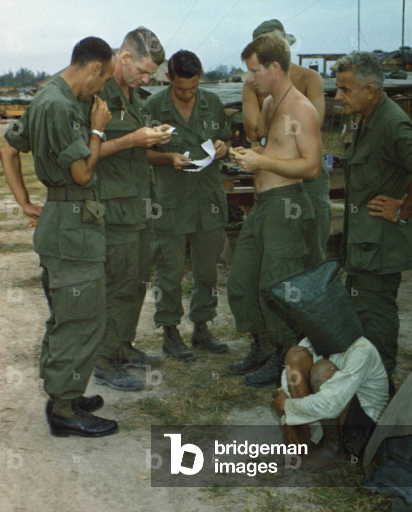 Vietnam War. A suspected Viet Cong sits on the ground with a black bag over his head while several US soldiers examine papers. He was captured during an attack on an American outpost near the Cambodian border in South Vietnam. Dec. 20, 1968
