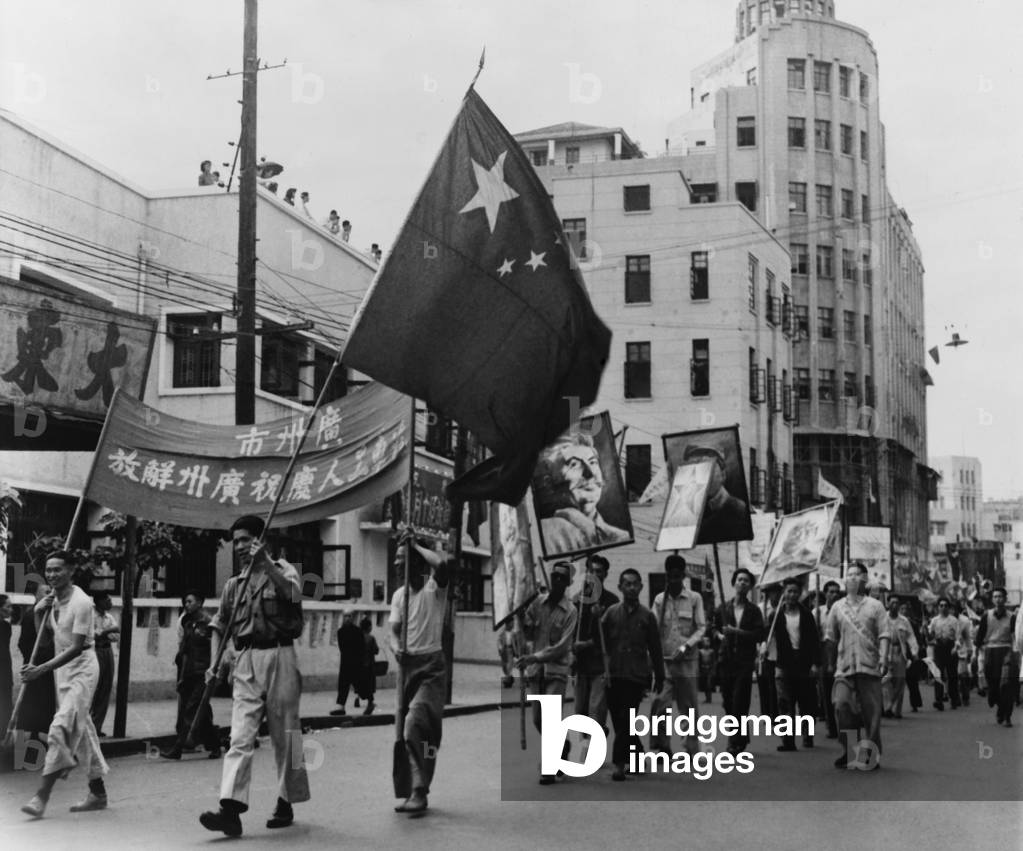 Communist marchers parade along the Pearl River waterfront in Canton (Guangzhou), China. They carry signs with portraits of Stalin and Chinese Communist leaders. 1949.