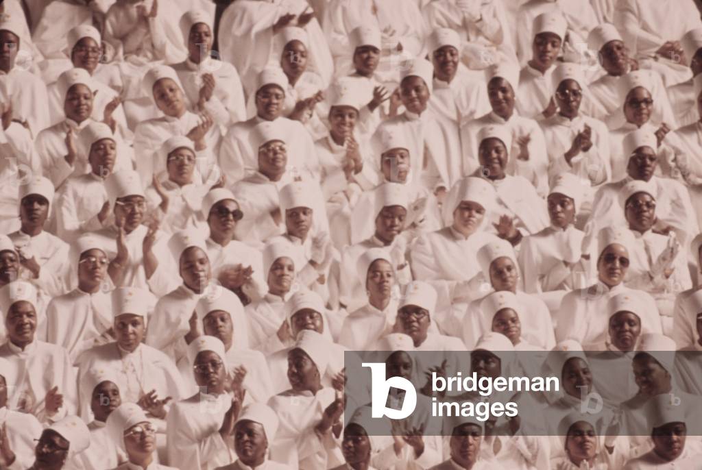 Black Muslim women dressed in white applaud Elijah Muhammad's Annual Savior's Day message. March 1974