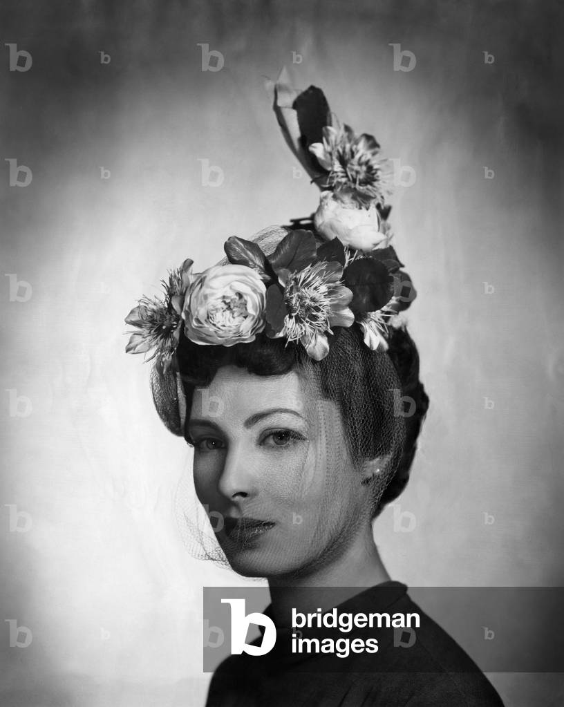 A model wearing a hat by Lilly Dache made of gray linen straw with yellow roses and passion flowers and a light veil under the chin. From Lilly Dache's Spring 1948 collection