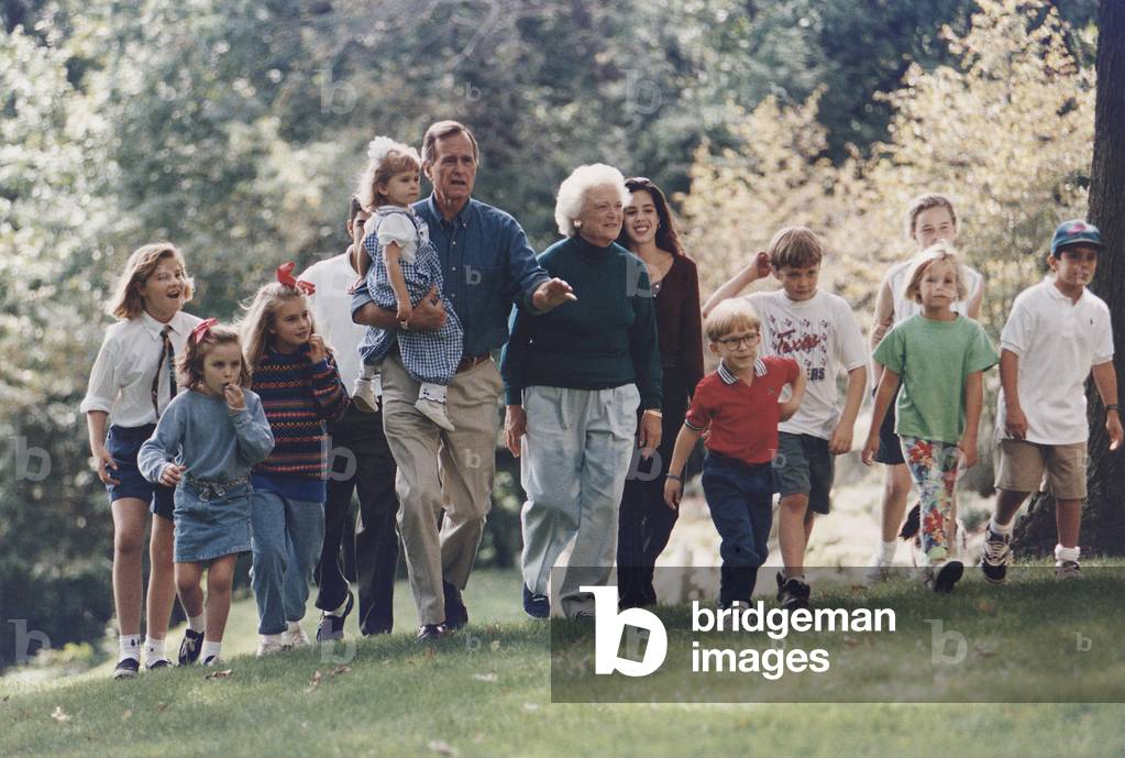 President George H. W. Bush and wife Barbara walk with eleven of their grandchildren at the presidential retreat Camp David. c. 1991 (photo)