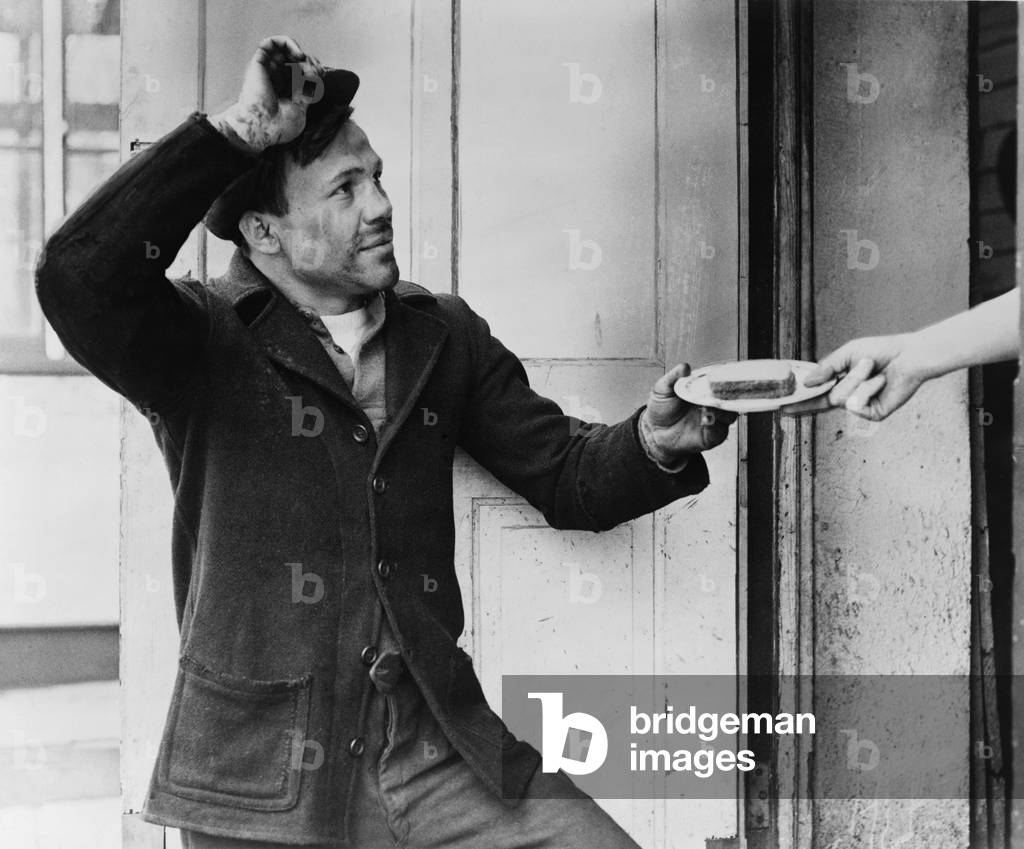 A Hobo, Lou Ambers, tips his hat as he accepts a sandwich from a woman's hand during the Great Depression. Unemployed men were more reluctant than women to live with their relatives, and many wandered as tramps looking for day labor and handouts. 1935