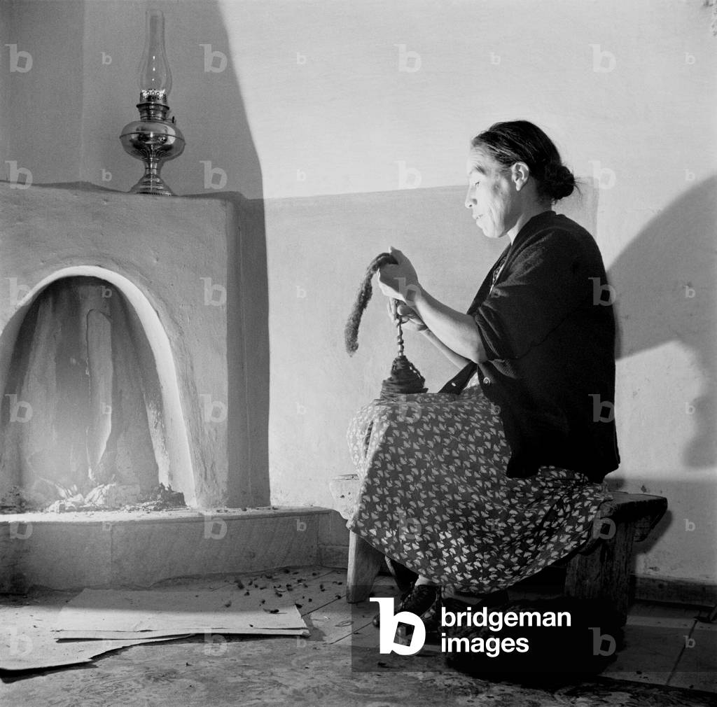 Spanish-American women, Maclovia Lopez, hand spinning wool by the light of the fire in New Mexico's Taos County. New Mexico has a four century tradition of wool production and weaving