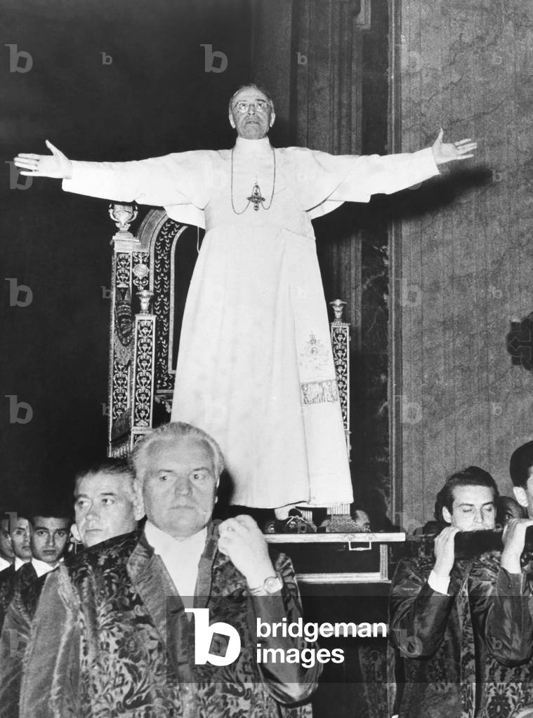 Pope Pius XII standing before his Sedia Gestatoria, a portable throne carried by twelve footmen. July 19, 1951. He was carried into one of the Vatican's Apostolic Halls to bless pilgrims