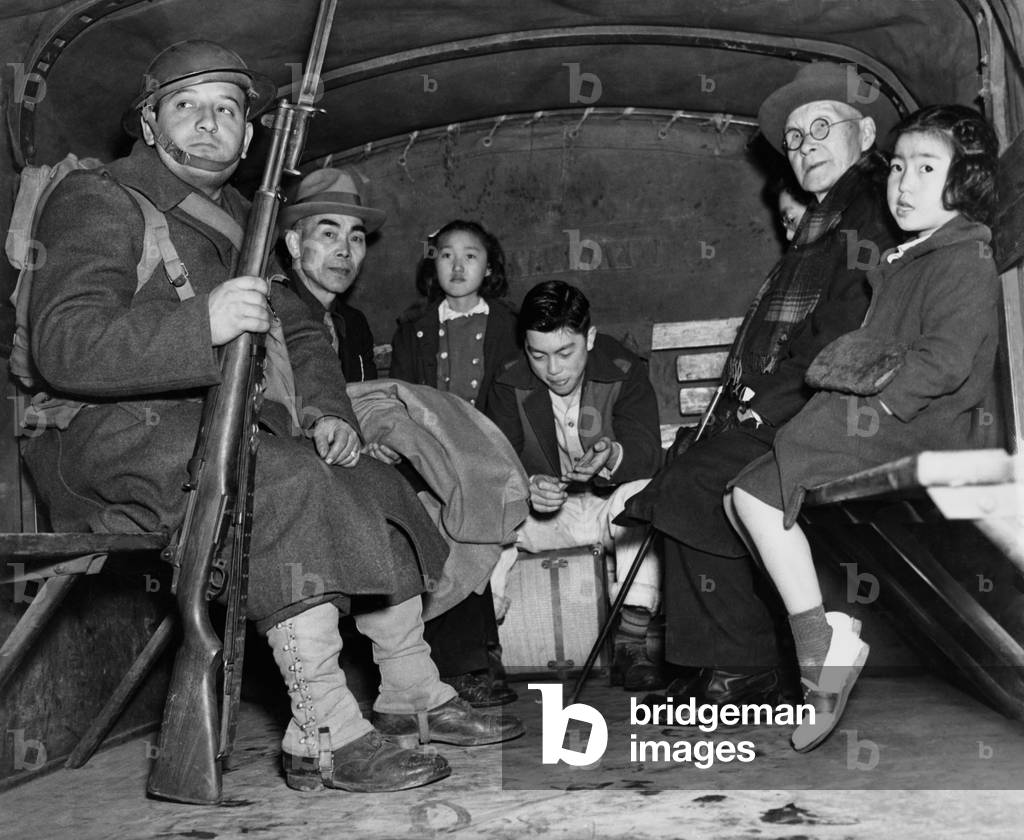Under armed guard, parentless children and a pastor sit in the back of truck for their evacuation from Bainbridge Island, during the World War II internment of Japanese Americans. The orphans were interned at Manzanar's 'Children's Village,' the only orphanage in internment camps, to which 100 children from Alaska to San Diego were sent for the duration of the war. 1942