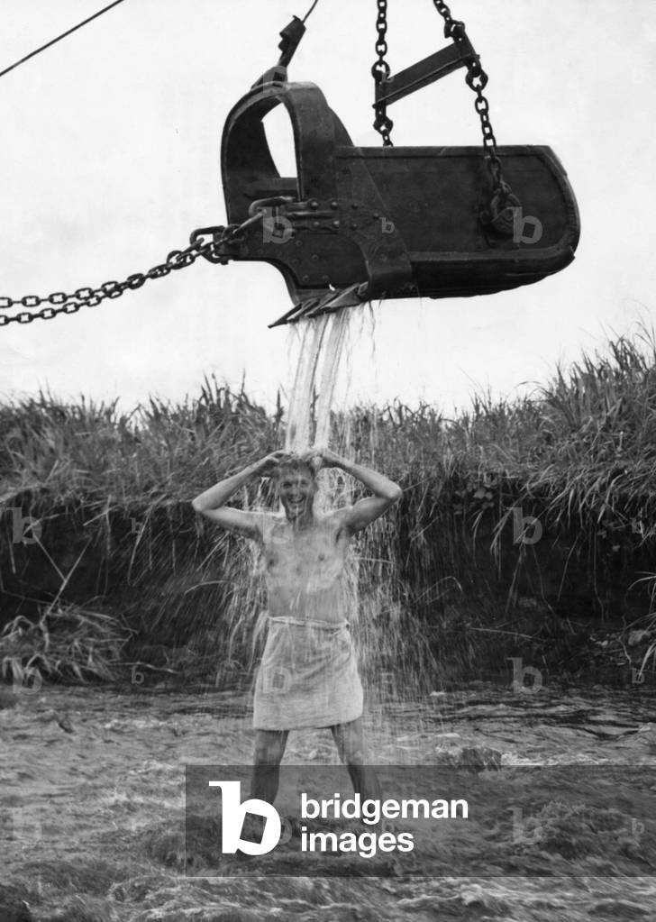 U.S. Marine officer enjoys an early morning shower at Cape Gloucester on New Britain. Water is provided by friendly steam shovel operator, May 10, 1944.
