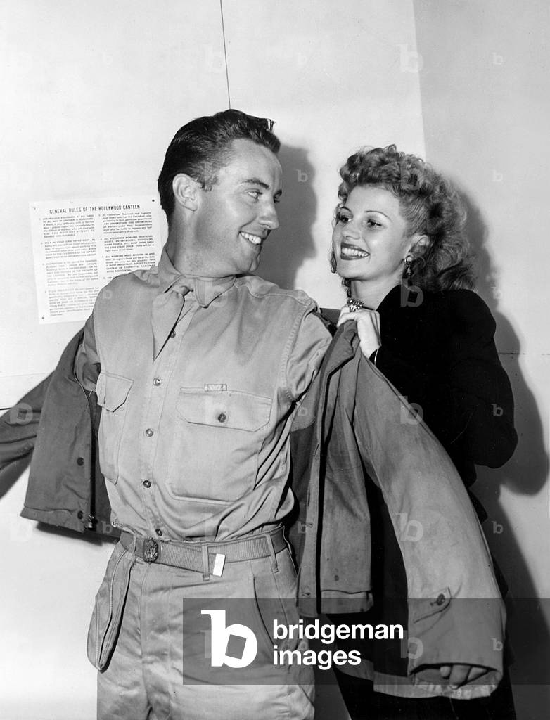 Rita Hayworth helps a lucky soldier into his jacket at the Hollywood Canteen, 1943