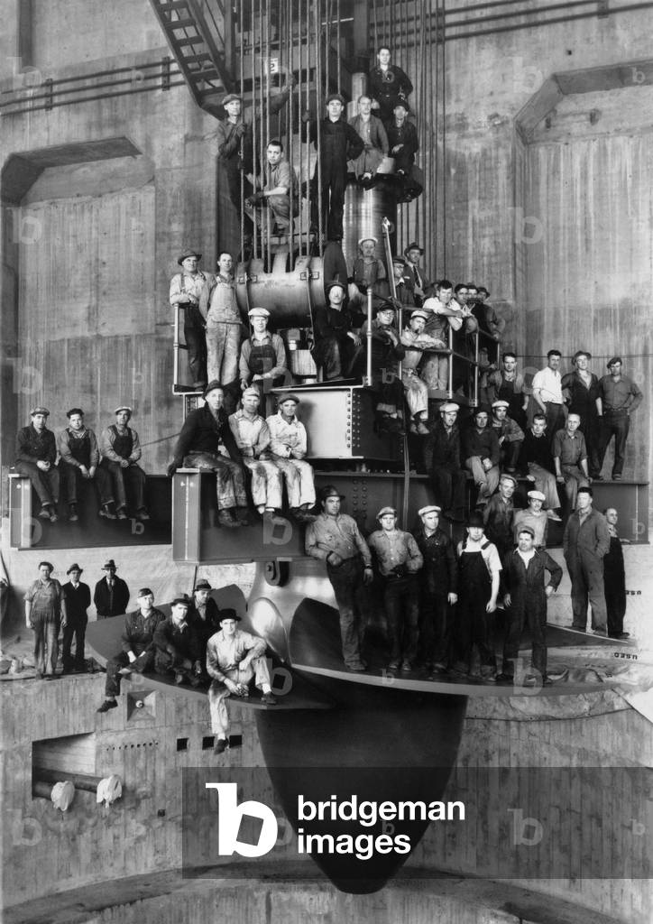 Workmen pose for a group portrait on the giant turbine in the powerhouse of the Bonneville Dam. c. 1937