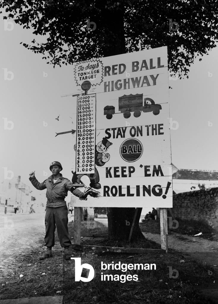 U.S. MP waves on a 'Red Ball Express' motor convoy near Alencon, France, Sept. 5, 1944. While Atlantic ports and French railroads were repaired, French highways were commandeered for military vehicles from Aug. 25, 1944 until Nov. 16, 1944. African American soldiers loaded and drove 50% of trucks of the vital supply line