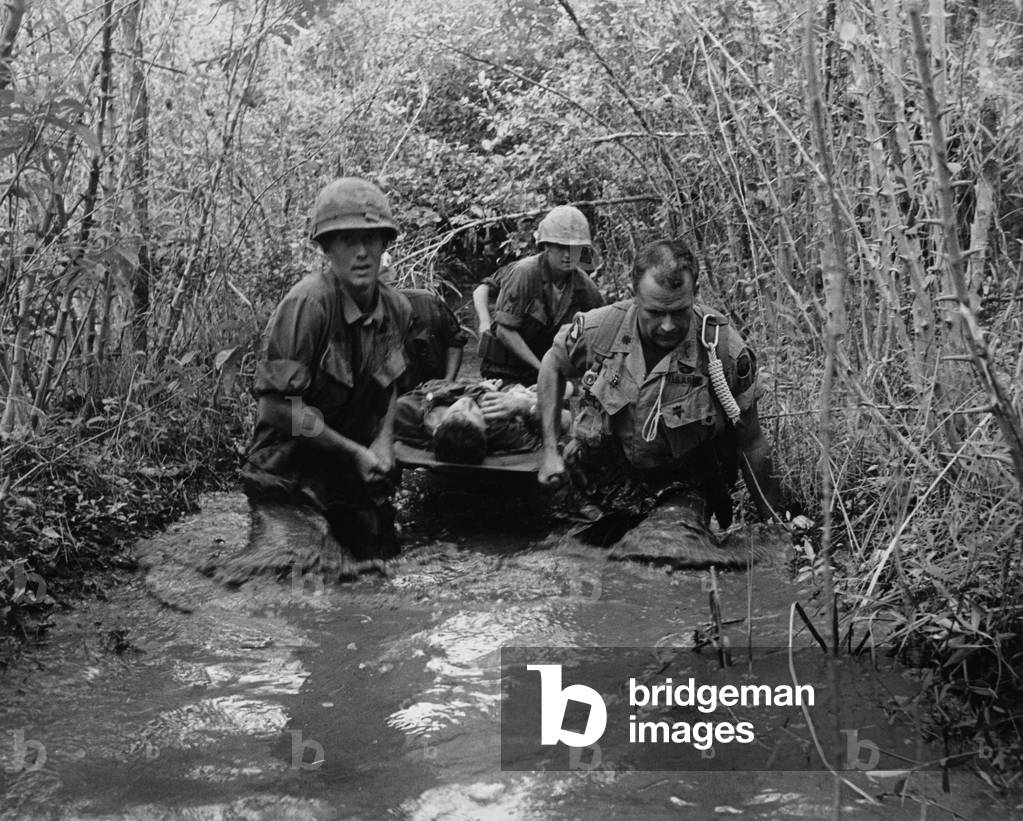 Vietnam War. US Soldiers carry a wounded comrade through a swampy area. 1969