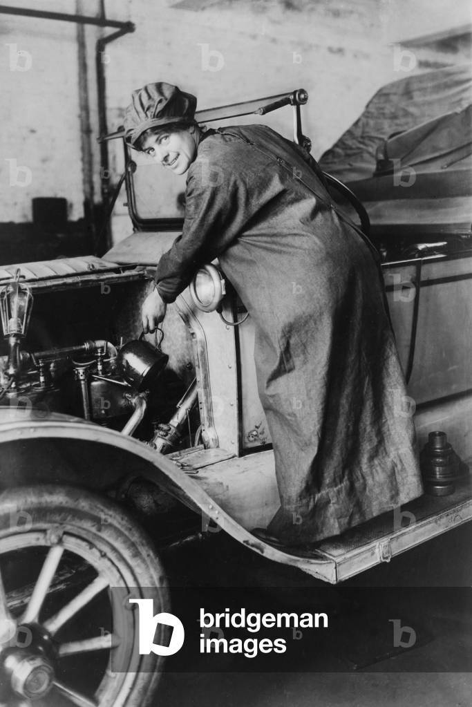 Female auto saleswoman, Rosalie Jones, attends to auto mechanics in a duster and hat in 1925