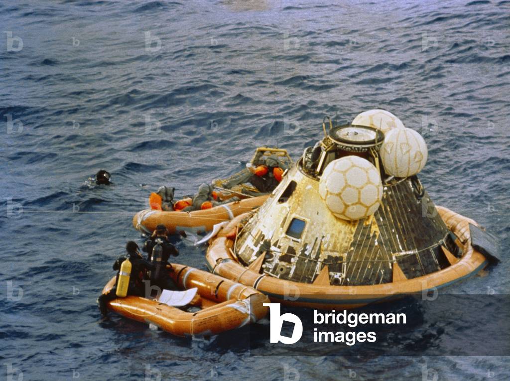 Apollo 11 Recovery. Behind the floating Command Module the astronauts are dressed in Biological Isolation Garments for their transfer to the quarantine trailer on the USS Hornet