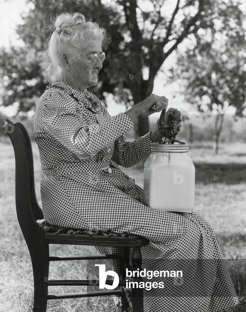Elderly farm woman using a small glass butter churn. Oklahoma, July 1935