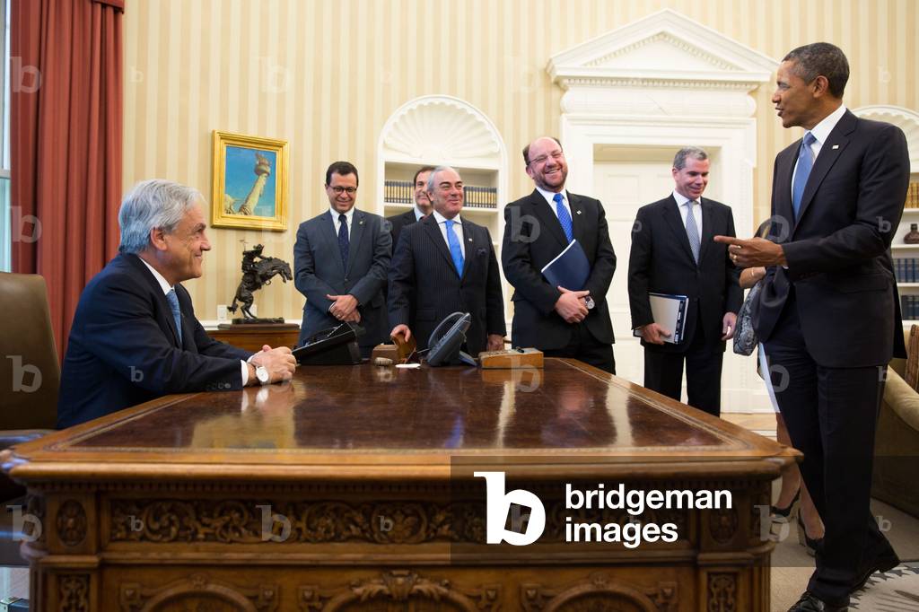 President Sebastian Pinera of Chile sits at the Obama's Resolute Desk in the Oval Office. The Chilean delegates share the good humor. June 4, 2013