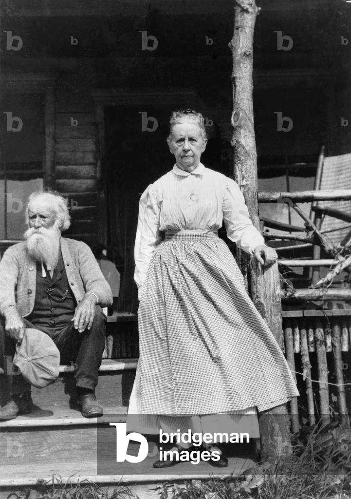 John Burroughs (1837-1921), American naturalist author seated on steps of house with his wife standing. 1915