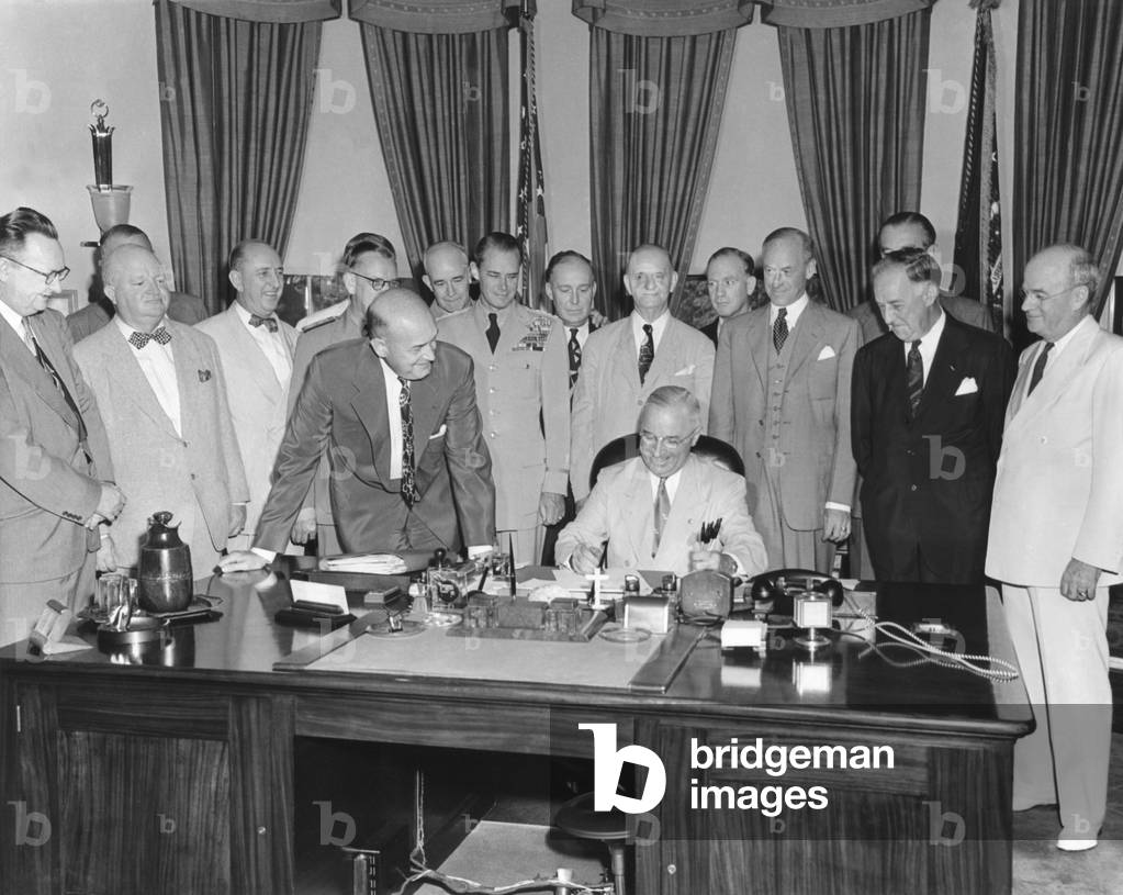 President Harry Truman signing H.R. 5632, the National Security Act Amendments of 1949. The law converted the National Military Establishment into a new Department of Defense. Aug. 10, 1949. L to R: Sen. Virgil Chapman; no ID; Sen. Richard Russell; Adm. Louis Denfelt; Sen. Leverett Saltonstall; Defense Sec. Louis Johnson (leaning over the desk); Gen. Omar Bradley; Gen. Hoyt Vandenberg; Rep. Dewey Short; Rep. Carl Vinson; Army Sec. Gordon Gray, Sen. Millard Tydings, AF Sec. Stuart Symington; Under Defense Sec. Stephen Early, and Navy Sec. Francis Matthews.
