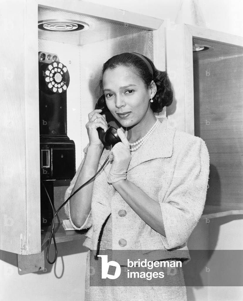 Dorothy Dandridge (1922-1965), half-length portrait, standing, facing left, holding telephone receiver at New York's airport in 1959, the year she starred in PORGY AND BESS