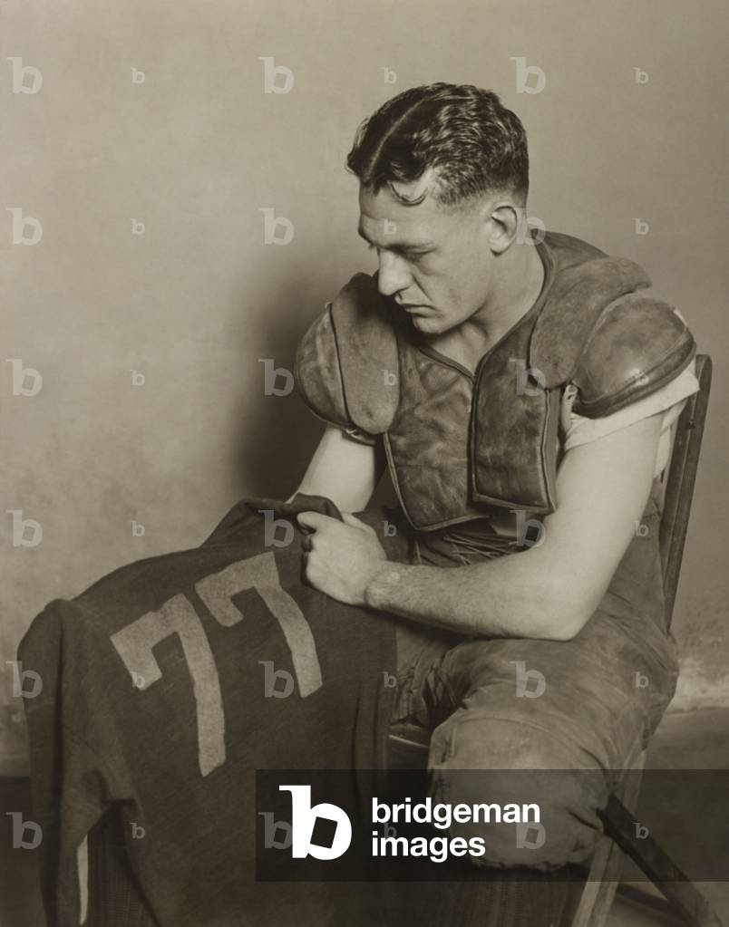 Harold 'Red' Grange holding his football jersey number. His number 77 was retired at the University of Illinois in 1925.